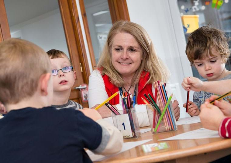 A teacher sits, smiling, with her students