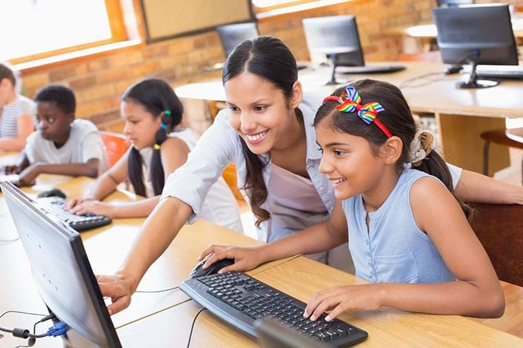 A teacher helps her student on a PC