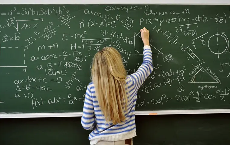 Student writing maths equations on a chalkboard.