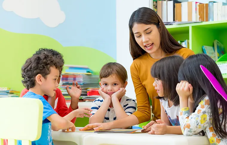 A teacher reading to a group of young children at a table in a classroom.