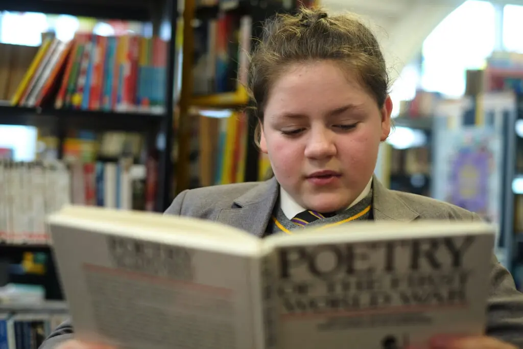 Teenage student in school uniform reading in a library.