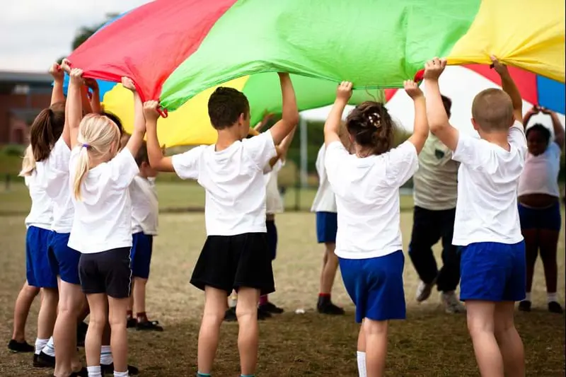 Children in gym clothes holding a colorful parachute.