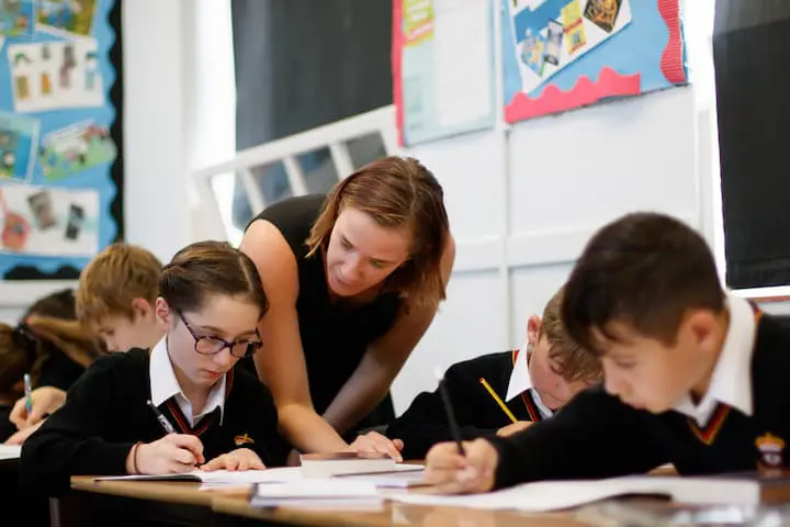 Teacher helping students with classwork in a classroom.