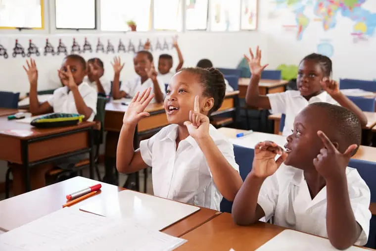 Enthusiastic primary school students in a classroom raising their hands.