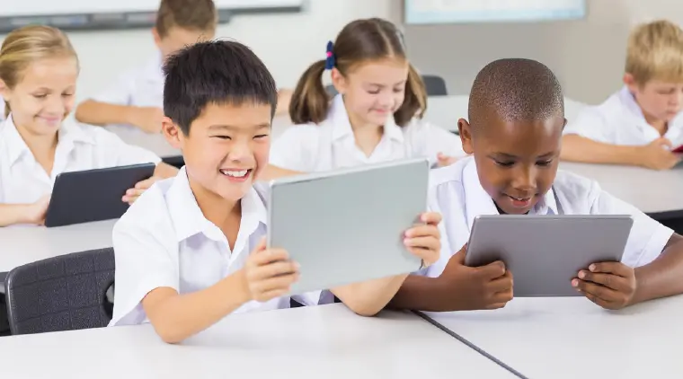Primary school students in uniform use tablets in a classroom.