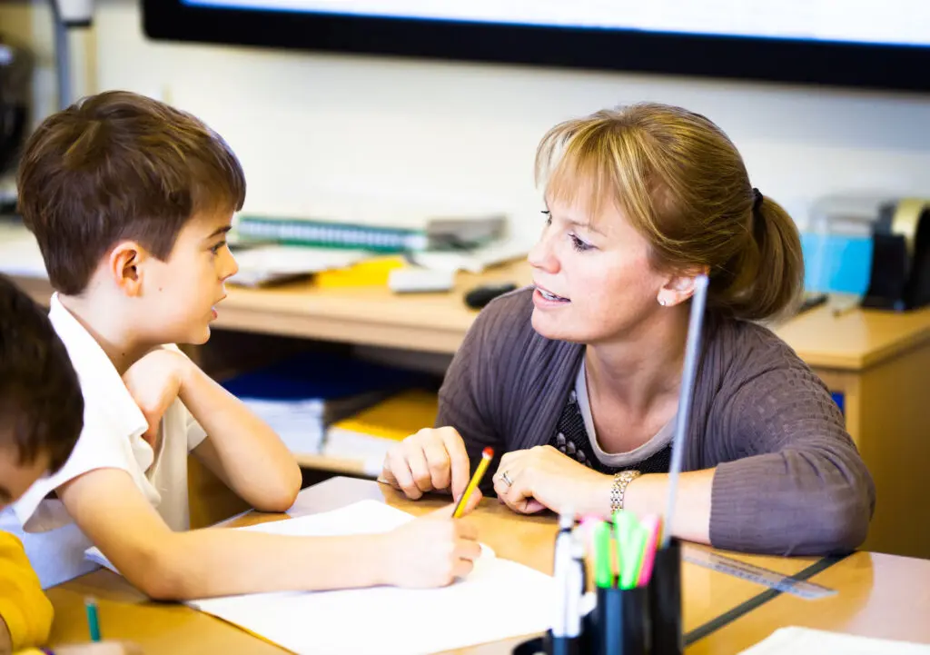 A teacher helping a student with their schoolwork at a desk.