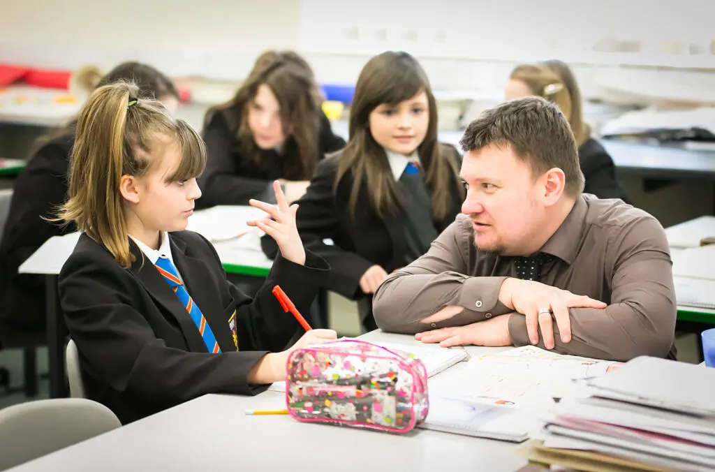 Teacher discussing schoolwork with a student at their desk.
