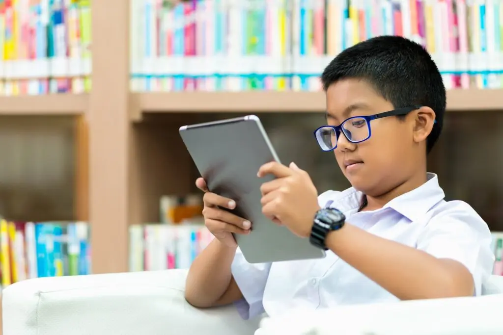 Boy in school uniform reading a tablet in a library.