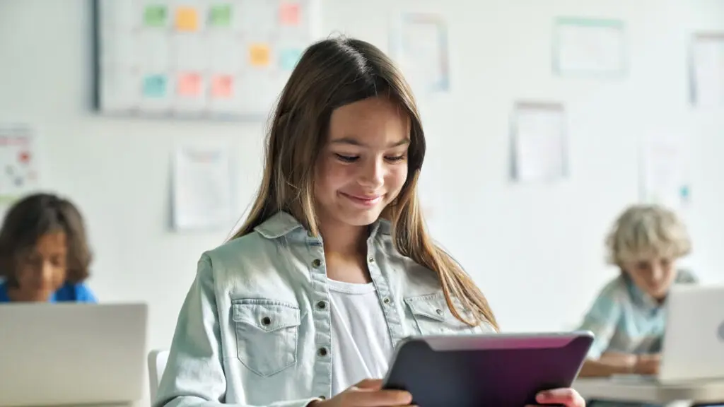 A girl smiling while using a tablet in a classroom.