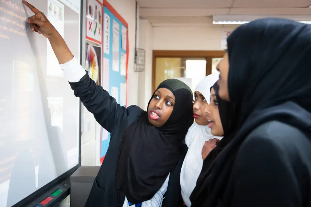 A student pointing to a smartboard as classmates look on.