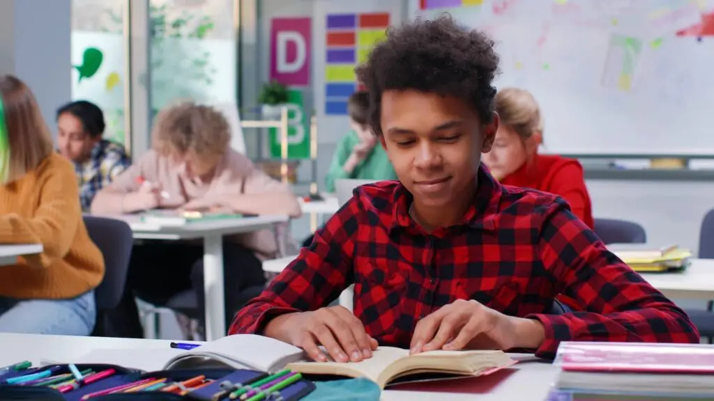 Teenage boy reading a book in a classroom.