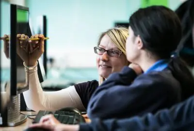 Teacher helping a student with computer work.